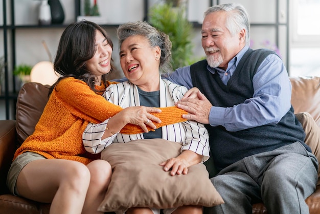 Free photo happiness asian family candid of daughter hug grandparent mother farther senior elder cozy relax on sofa couch surprise visiting in living room at hometogether hug cheerful asian family at home
