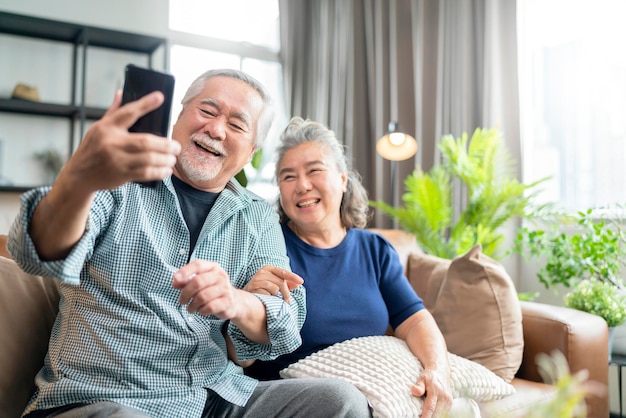 Free photo happiness asian old senior retired couple enjoy videocall to family together on sofa in living room at homeasian people use smartphone communication to family home isolation ides concept